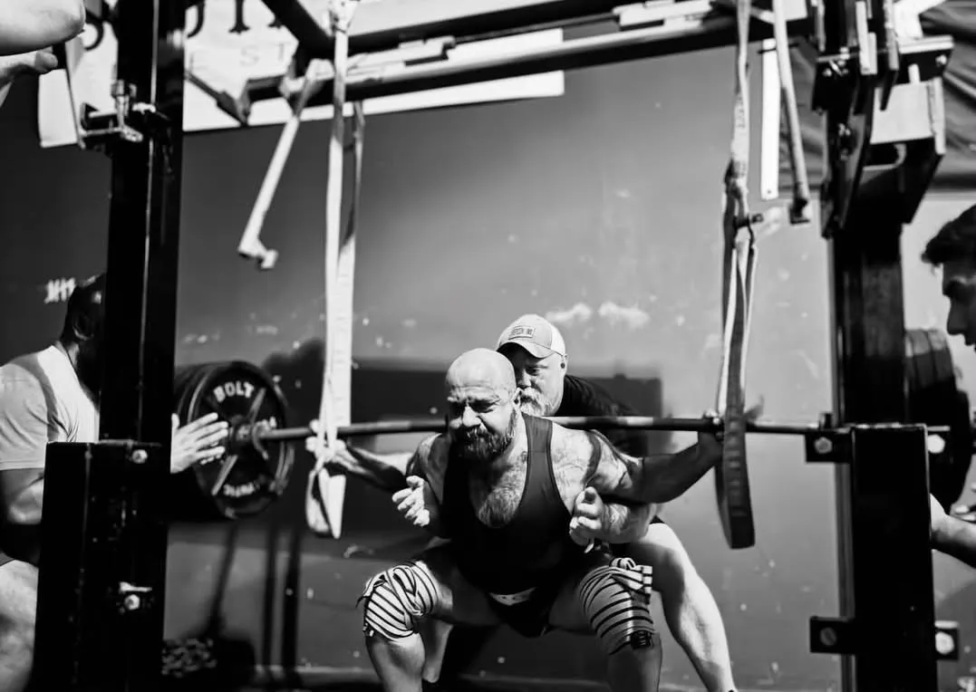 A lifter mid-squat, spotters either side of the bar