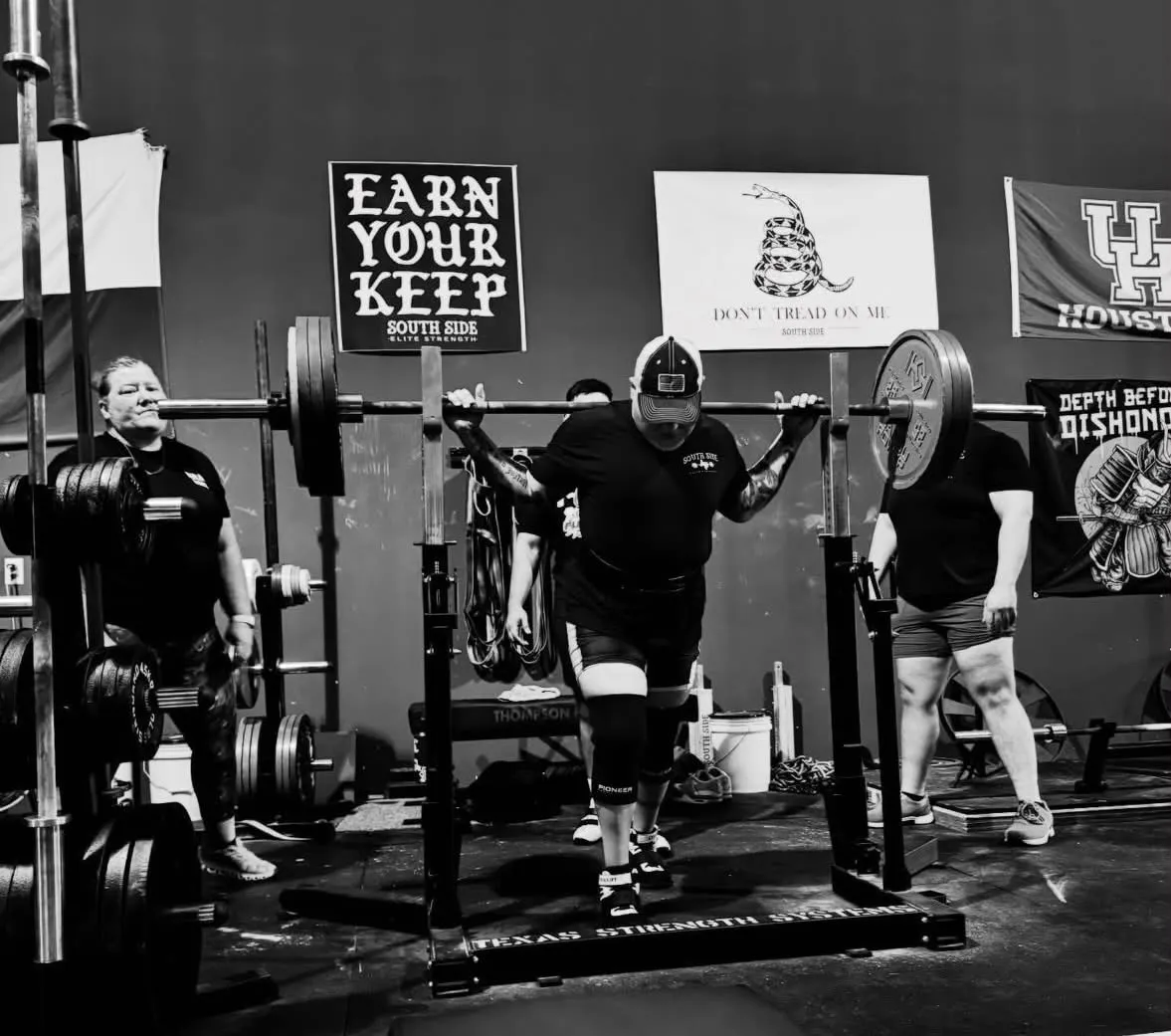 A lifter unracking a loaded squat bar beneath the gym's Earn Your Keep banner
