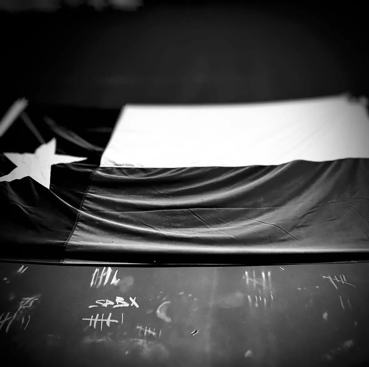A Texas flag over a bench, chalk tally marks scratched into the top